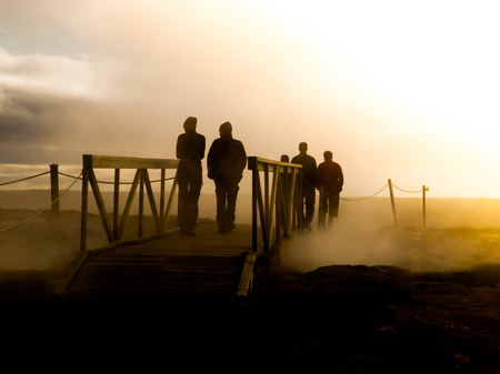 Group of people walking over bridge in geothermal area. Only silhouettes are visible.の写真素材