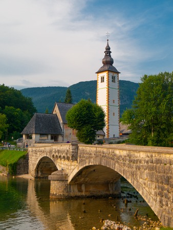 Church tower and stone bridge at Lake Bohinj in alpine village Ribicev Laz, Sloveniaの写真素材