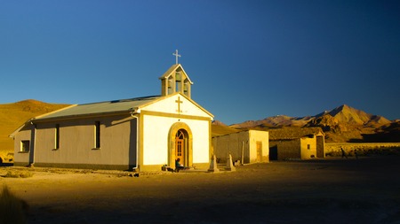Small white church and woman sitting in front of it in Cordillera de Lipez in southern bolivian Altiplano. The church looks like from western movie.の写真素材