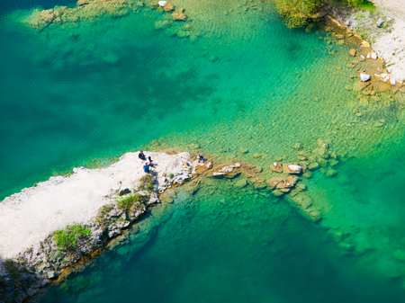 Rocky ness in blue azure water ang group of people having a picnic on itの写真素材