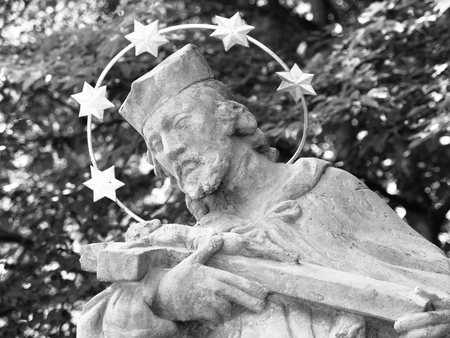 Detailed view of statue of saint with halo and green trees on background. Black and white image.の写真素材