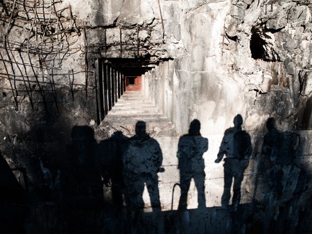 Loophole in old military bunker and shadows of men on devasted wallの写真素材