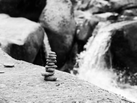 Balanced pebble stone pyramid with unfocused river waterfall on background . Black and white image.の写真素材