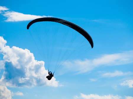Dark paraglide silhouette on background of blue summer sky and white clouds. Adrenalin sport theme.の写真素材