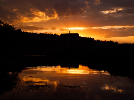 Mountain sunset with river reflection and dark silhouette of forest and rooftop, Jizerka village, Jizera Mountains, Czech Republicの写真素材
