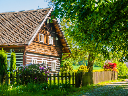 Old traditional timbered cottage with romantic and idyllic lush green flower garden with wooden fence on sunny summer day. Czech rural architecture.の写真素材