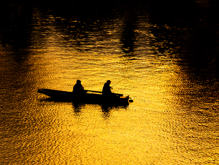 Boat with 2 men fishing in the river. Black silhouette on sunset sky reflection background.の写真素材