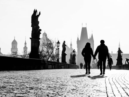 Foggy morning on Charles Bridge, Prague, Czech Republic. Sunrise with silhouettes of walking people, statues and Old Town towers. Romantic travel destionation. Black and white image.の写真素材