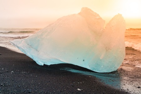 Icebergs sphashed by sea waves on black beach at sunrise time near Jokulsarlon glacier lake, Iceland.の写真素材