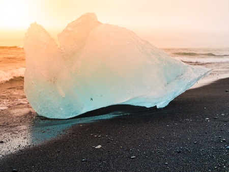 Icebergs sphashed by sea waves on black beach at sunrise time near Jokulsarlon glacier lake, Iceland.の写真素材