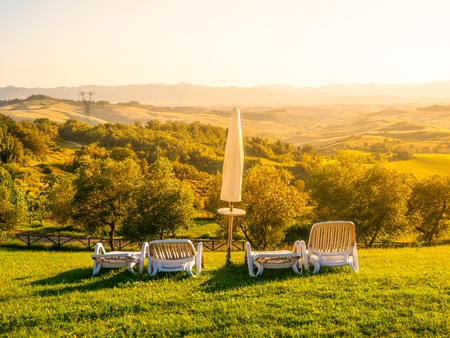 Beautiful rest place with umbrellas and sunbeds in Tuscan landscape. Evening summer sunset. Italy.の写真素材