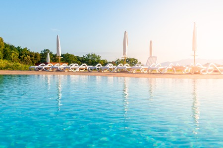 Beautiful luxury swimming pool with bright blue water, umbrellas and sunbeds in Tuscan landscape. Evening summer sunset. Italy.の写真素材