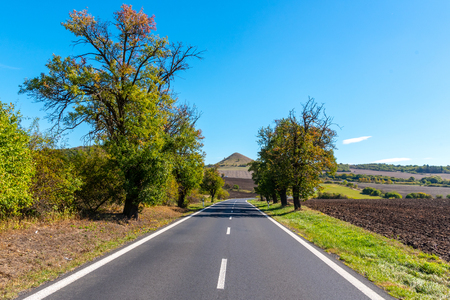 Asphalt road and typical conical volcanic hill of Central Bohemian Highlands on sunny summer day, Czech Republic.の写真素材