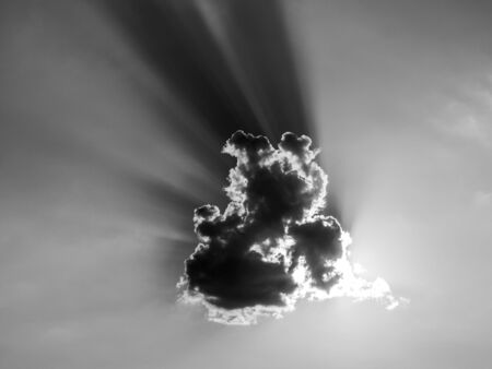 Sun rays from the evening sun behind small cloud. Black and white image.の写真素材