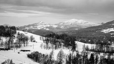 Snowy winter hilly landscape. Beautiful rural range. Panorama with Kytlice village in Lusatian Mountains, Czech Republic. Black and white image.の写真素材
