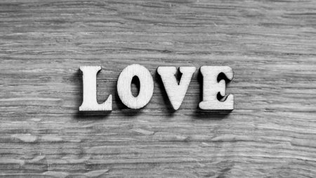 Love - word inscription of 3D wooden letters on the wood textured board background. Expression of romantic theme or Valentines Day. Rustic style inscription. Black and white image.の写真素材
