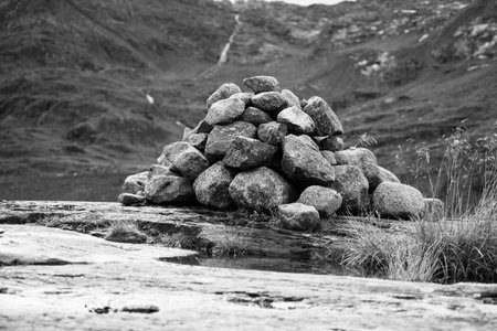 A carefully stacked cairn stands on a rocky terrain with lush greenery and a waterfall background....