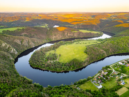 Aerial view of the Solenice Horseshoe Bend on the Vltava River in Czechia, showcasing the winding river surrounded by lush greenery and a small village during a picturesque sunset.の写真素材