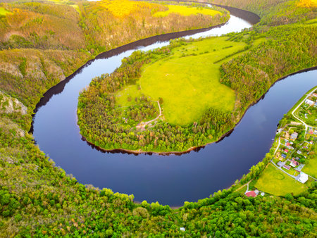 An aerial view captures the vibrant Horseshoe Bend on the Vltava River in Solenice, Czechia. The river curves dramatically through lush green landscapes under a clear sky.の写真素材