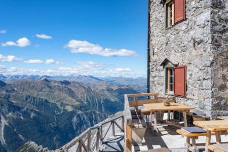 A tranquil scene at the Julius Payer House, showcasing a terrace with wooden benches and tables, affording visitors breathtaking views of the Italian Eastern Alps. Ortles Mountain, Italyの写真素材