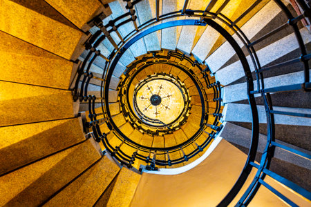 A view from the bottom of a winding staircase, looking up toward a chandelier. The staircase...