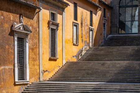 Visitors ascend the grand staircase at Capitoline Square in Rome, Italy, surrounded by vivid orange walls and architectural details typical of the historic district.の写真素材