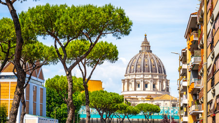 A picturesque view of St. Peters Basilica showcases its grand dome amidst a charming street. Lush trees frame the basilica, creating a serene atmosphere in Vatican City.の写真素材