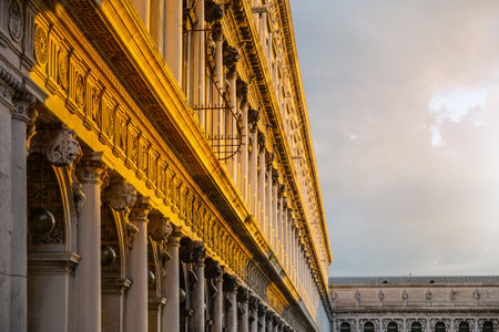The intricate architectural features of the New Procuracie in Venice are highlighted by the warm glow of the setting sun, showcasing columns and ornate designs against a dramatic sky.の写真素材