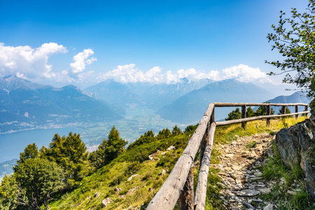 A breathtaking panorama reveals Lake Como nestled between lush hills, framed by majestic mountains and clear blue skies. Natures beauty captivates visitors exploring the scenic trails.の写真素材