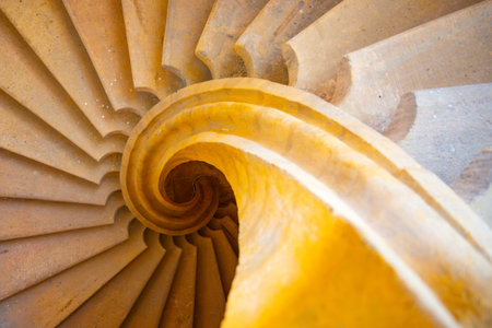 A stunning helical staircase with smooth, yellow steps spirals downwards. Its intricate design...