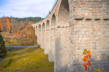 On a sunny autumn day, the impressive railway viaduct in Smrzovka stands tall against a backdrop of colorful foliage in the Jizera Mountains, inviting travelers to explore the stunning landscape.の写真素材