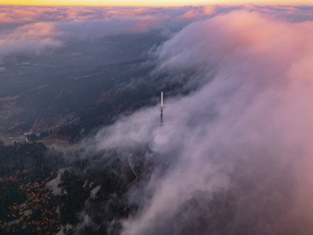 Dramatic clouds envelop the scenery during a vibrant sunset in Liberec, Czechia, highlighting the tower rising above the misty landscape, creating an enchanting atmosphere.の写真素材