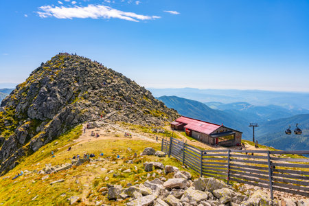 Visitors relax and enjoy breathtaking views atop Chopok Mountain in the Low Tatras, Slovakia. The sunny day highlights the rocky terrain and picturesque cabin nearby.の写真素材