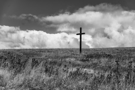 A stark wooden cross rises from a grassy meadow in the Ore Mountains near Haj, Czechia. The serene landscape is accentuated by dramatic clouds in the background.の写真素材