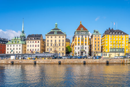Vibrant buildings in Stockholms old town reflect in the calm water, showcasing rich architectural styles under a clear blue sky, inviting exploration and admiration from visitors.の写真素材