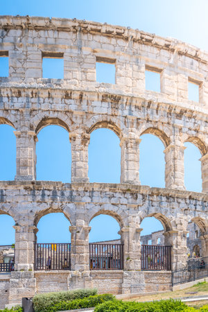 The Roman amphitheatre in Pula stands as a monumental reminder of ancient architecture. Visitors admire its impressive structure under a clear blue sky, showcasing its historical significance.の写真素材