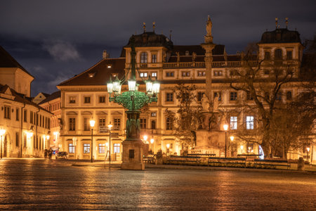 At evening, a historic lamppost illuminates Hradcanske Square in Prague, highlighting architectural details and creating a warm atmosphere among the surrounding buildings.の写真素材