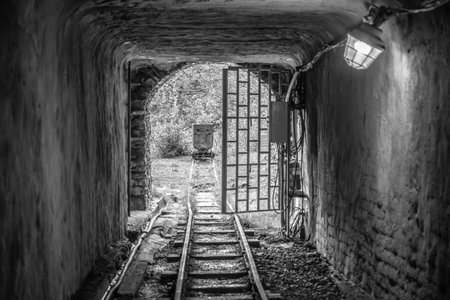 The entrance to a mine shaft in Jachymov features an open gate revealing track lines leading deeper underground. Soft light illuminates the rustic stone walls, enhancing the mysterious atmosphere.の写真素材