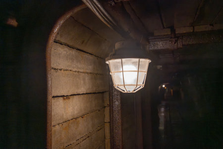 A vintage mine shaft lamp hangs from the tunnel ceiling, casting a warm glow on the rough wooden walls. This lamp represents the mining history of the area, providing light in underground depths.の写真素材