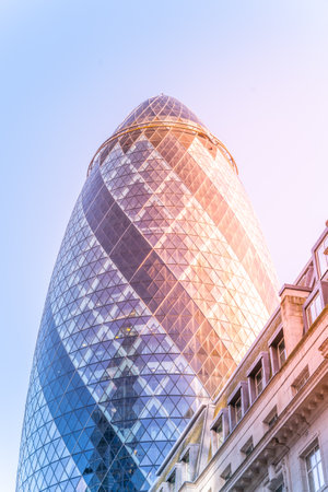 Gherkin skyscraper, an iconic landmark in Londons financial district, showcases unique architecture with a stunning glass facade reflecting the sky and nearby buildings during sunset.の写真素材