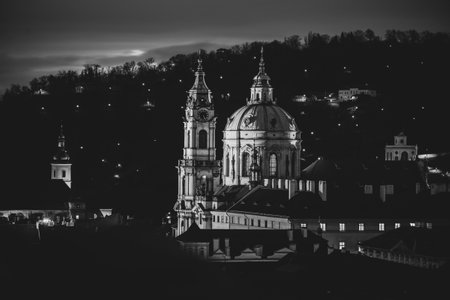 Nestled in the Lesser Town of Prague, St Nicholas Church showcases stunning Baroque architecture, beautifully lit against the night sky, surrounded by the tranquility of the historic landscape.の写真素材