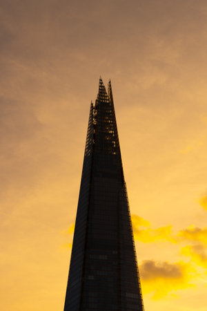 The Shard skyscraper stands tall against a vibrant sunset in London, casting its distinctive silhouette. The warm hues highlight the architectural elegance of this landmark.の写真素材