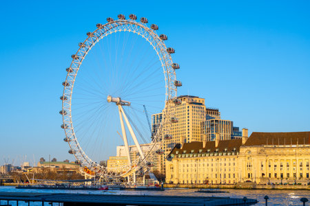 A large observation wheel stands tall against a clear blue sky, providing breathtaking views of the London skyline and the River Thames. Tourists enjoy this iconic attraction from capsule rides.の写真素材
