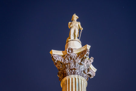 Nelsons Column stands tall in Trafalgar Square, beautifully illuminated against the night sky. The statue of Admiral Nelson commands attention, surrounded by historic architecture.の写真素材
