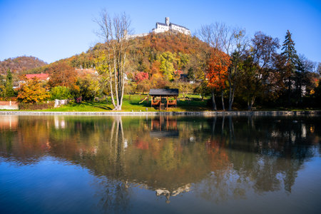 A serene autumn landscape featuring a medieval castle atop a hill, surrounded by colorful foliage and mirrored in the calm waters below, showcasing the beauty of the countryside.の写真素材