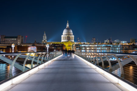 The Millennium Bridge spans the River Thames, illuminated under the evening sky. St. Pauls Cathedral stands majestically in the background, surrounded by city lights.の写真素材