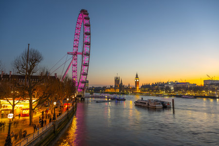 As twilight descends over London, the London Eye glows in shades of pink, reflecting on the River Thames.の写真素材