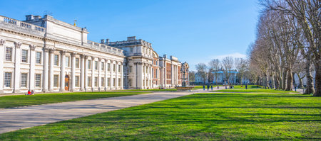 Visitors stroll along the spacious lawns of the Old Royal Naval College in Greenwich, London. The clear blue sky enhances the beauty of the historic architecture and lush greenery.の写真素材