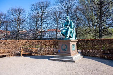 In Copenhagens Rosenborg Castle Gardens, visitors admire the bronze statue of Hans Christian Andersen. The setting is serene with benches and trees lining the pathways on a clear day.の写真素材