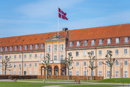 Rosenborg Barracks, located in Copenhagen, features distinct architectural elements and a prominent Danish flag waving under a clear blue sky. The landscape is inviting with well-maintained grounds.の写真素材